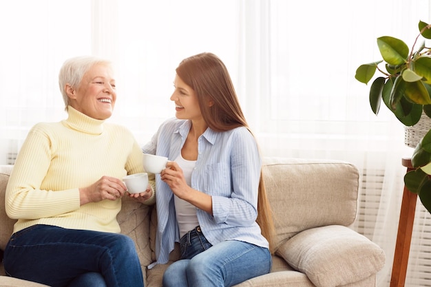 Young woman visiting senior mother and drinking coffee together