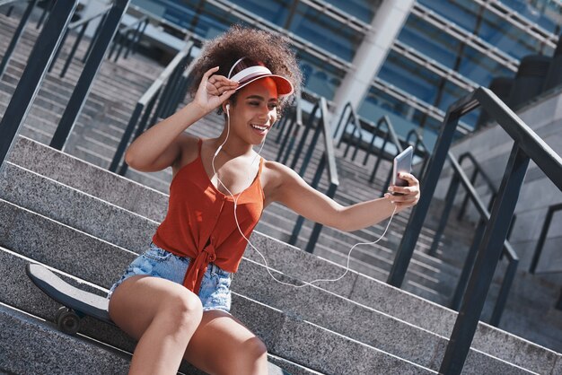 Young woman in visor and earphones free style on the street sitt