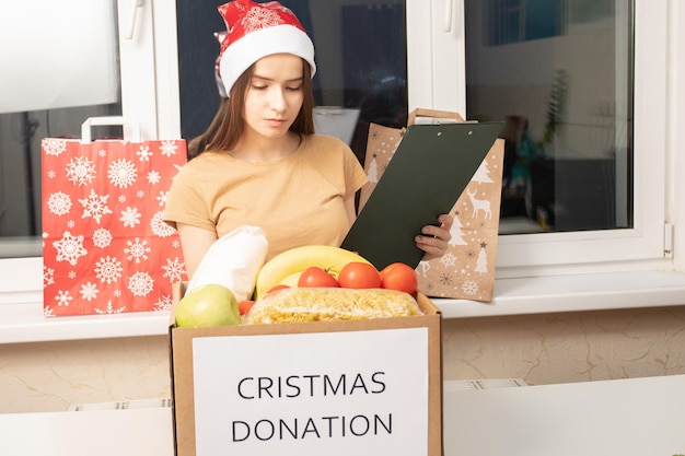 A young woman volunteer at a charity center packing groceries food in a donation box for Christmas for homeless poor people