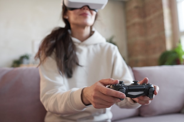 彼女の仮想ゲーム中にジョイスティックのボタンを押すVRメガネの若い女性