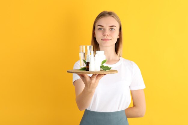 Young woman waiter holds tray with medicines on yellow background