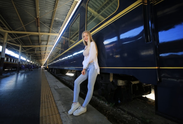 駅のホームでリラックスしてのんびりとヴィンテージ電車で待っている若い女性