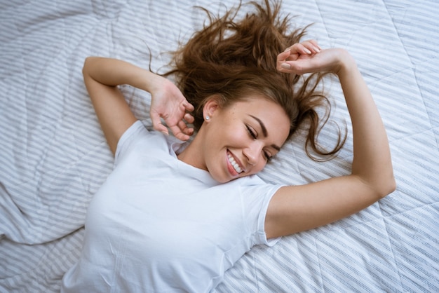 A young woman wakes up after a good nights sleep in her bed feelings of excitement happy woman in pa...