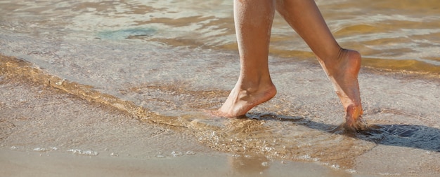 Молодая женщина, идущая по песчаному пляжу. Женские ножки в песке на берегу моря