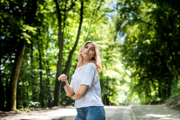 森の木々とアスファルト道路を歩く若い女性。自然を楽しみます