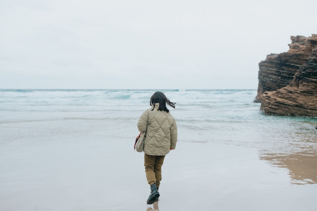 A young woman walking by the shore of the beach during a cloudy day