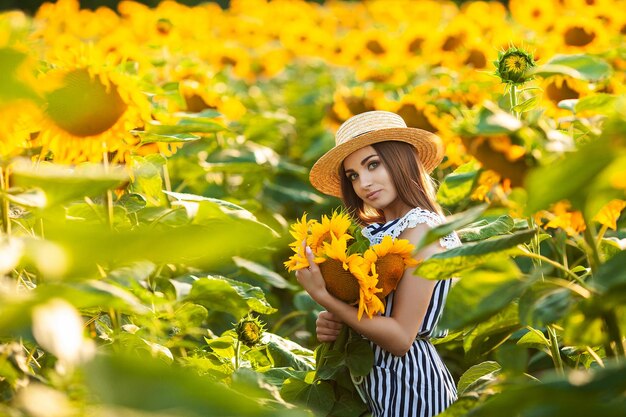 Young woman walking in the field toward the sun holding a sunflower