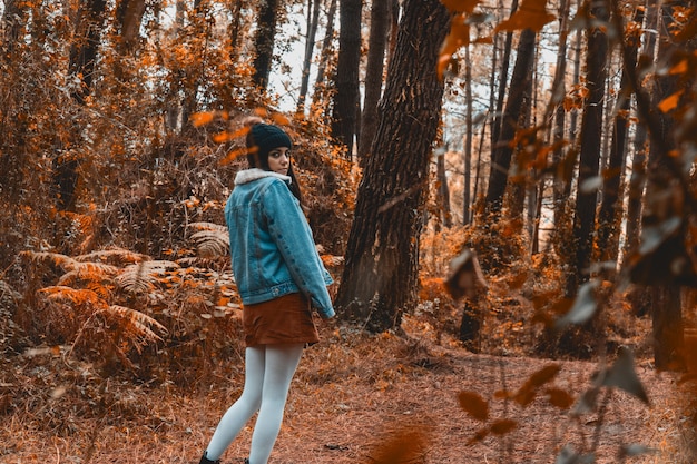 Young woman walking through a fall colors forest with season clothes