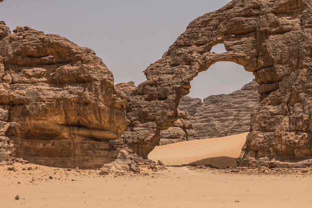 Young woman walking through stone arch in Sahara desert, Hoggar mountains, Djanet, Algeria