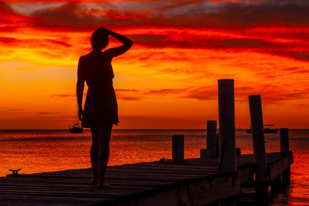 ウエストエンドビーチのオレンジ色の夕日でカリブ海に向かって歩いている若い女性