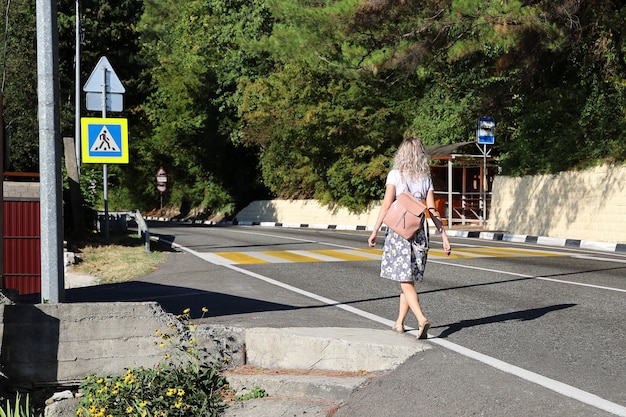 Young woman walks alone along deserted road towards the pedestrian crossing