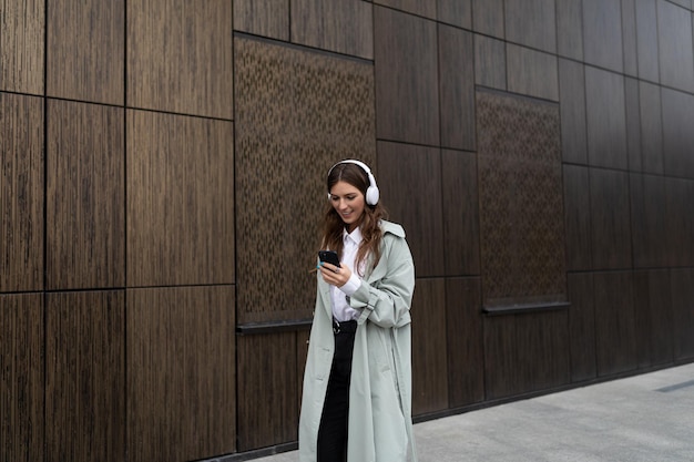 한 젊은 여성이 현대적인 건물의 갈색 벽을 배경으로 도시를 돌아다닌다