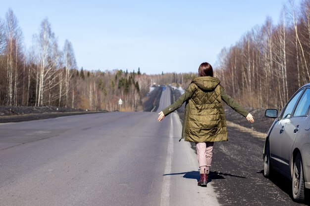 Молодая женщина идет по обочине дороги. Дорога в лесу.