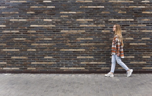Young woman walks down the street against a brick wall