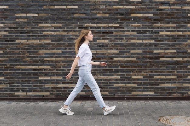 Young woman walks down the street in front of a brick wall