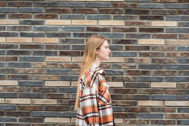 Young woman walks down the street in front of a brick wall