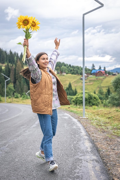 Una giovane donna cammina in montagna con un mazzo di girasoli