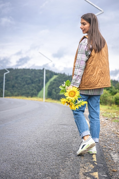 A young woman walks in the mountains with a bouquet of sunflowers