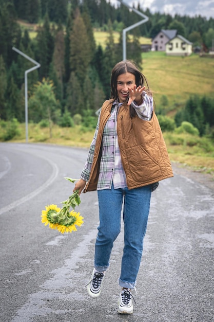 A young woman walks in the mountains with a bouquet of sunflowers