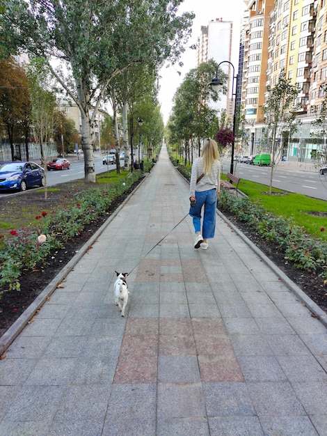 若い女性がジャック・ラッセル・テリアの犬を連れて公園の小道を歩いている