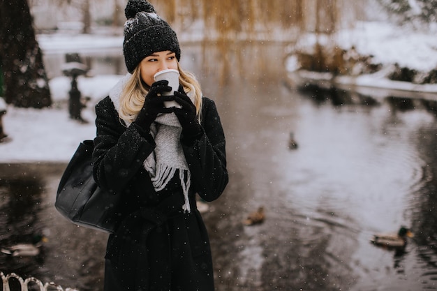 Giovane donna in vestiti caldi che gode nella neve con la tazza di caffè da asporto