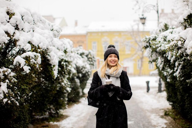 Young woman in warm clothes enjoying in snow with takeaway coffee cup