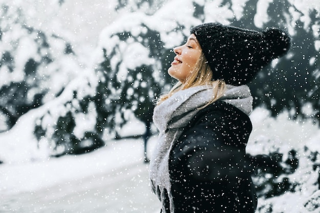 雪の中で楽しんでいる暖かい服装の若い女性