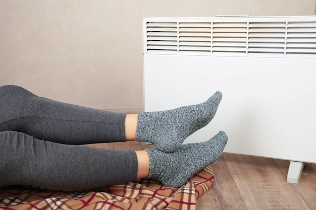 young woman in warm socks near electric heater at home concept of heating season top view