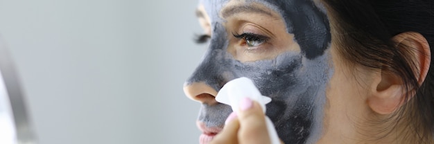 Young woman washes away black clay mask from face portrait. Home facial treatments concept.