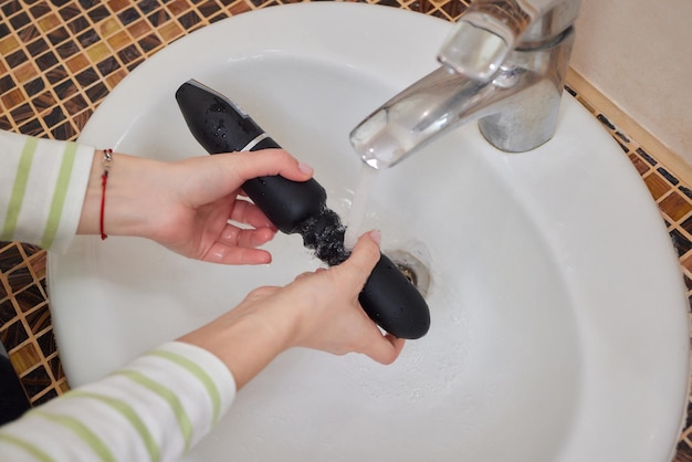 Young woman washes a sex toy in the sink at home