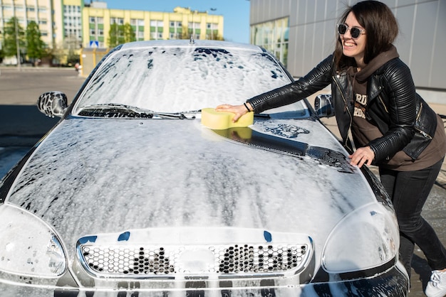 Молодая женщина моет машину на автомойке самообслуживания