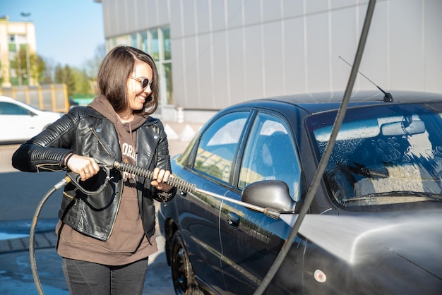 セルフサービス洗車で車を洗う若い女性