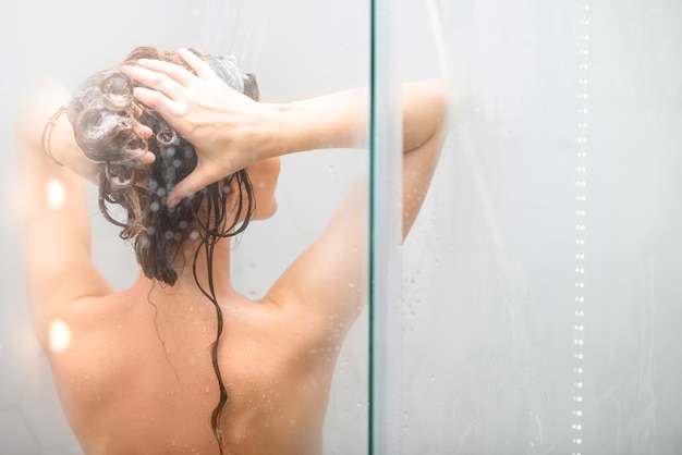 Молодая женщина, мытье волос с шанпу в душе. Вид сзади