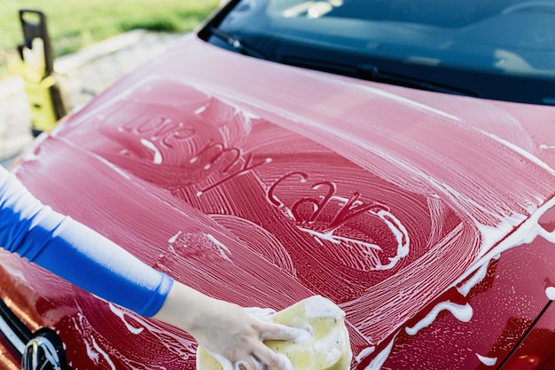 Young woman washing her car with sponge.