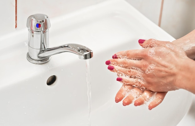 若い女性は石鹸で水道の蛇口の下で手を洗います。皮膚上の液体の詳細。個人衛生の概念