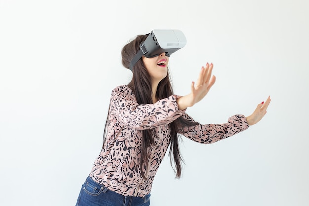 Young woman watches a movie with glasses of virtual reality standing on a white wall.