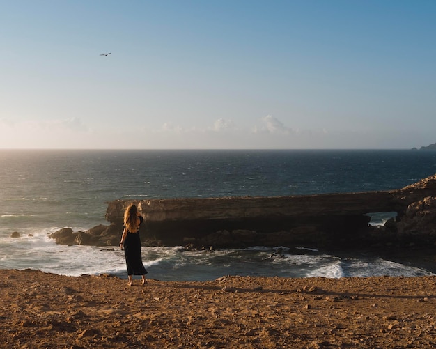 写真 若い女性は、夕暮れ時にフェルテベントゥラ島のいくつかの岩の崖から海を眺める