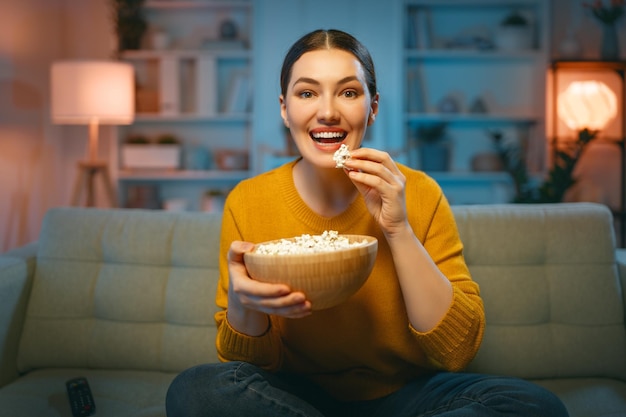 夕方にポップコーンとプロジェクターテレビ映画を見ている若い女性家で時間を過ごす女の子