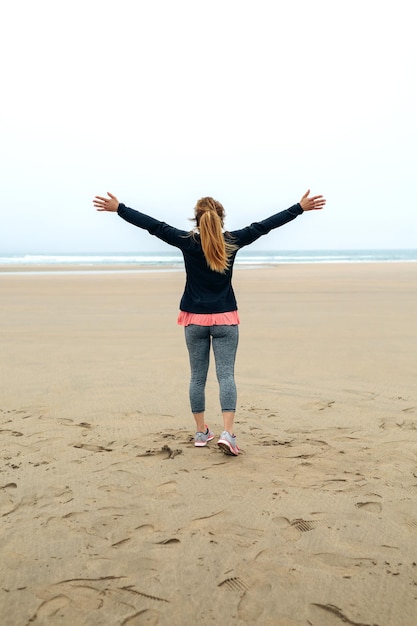 手を上げて秋の海を見ている若い女性