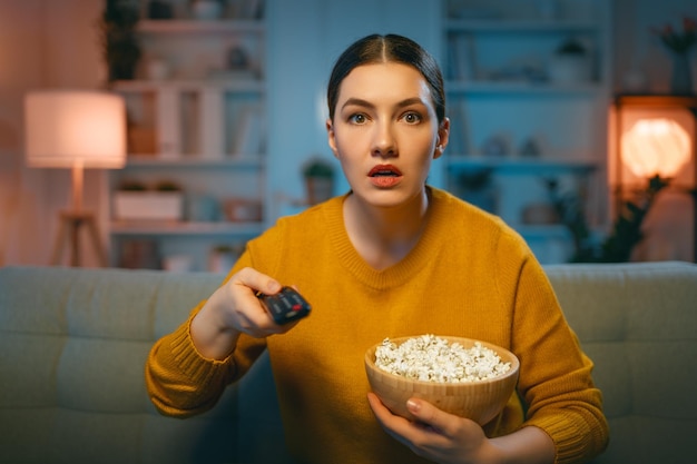 家で時間を過ごすポップコーンの女の子と一緒にテレビ映画を見ている若い女性