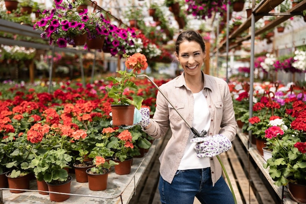 A young woman watering flowers and caring about them in a garden center or plant nursery.