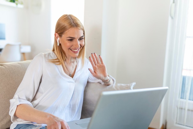 Young woman waving at laptop and talking to her friends via\
video call girl student talking by video conference call female\
teacher trainer tutoring by webcam online training ecoaching\
concept