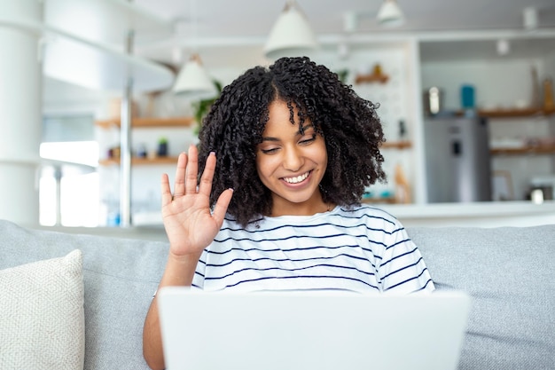 Young woman waving at laptop and talking to her friends via\
video call woman student talking by video conference call female\
teacher trainer tutoring by webcam online training ecoaching\
concept