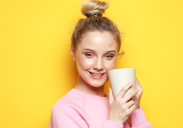 Photo young woman wear pink sweater with cute smile holding a cup of coffee over yellow background