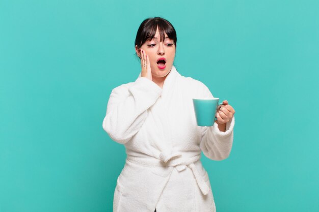 young woman wearing bathrobe feeling happy, excited and surprised, looking to the side with both hands on face