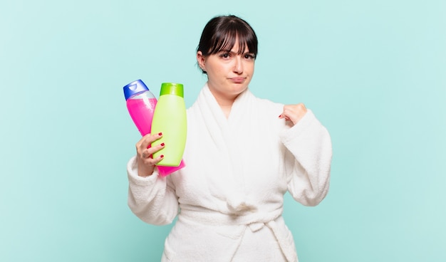 young woman wearing bathrobe looking arrogant, successful, positive and proud, pointing to self