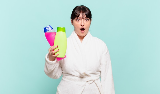 Young woman wearing bathrobe looking very shocked or surprised, staring with open mouth saying wow