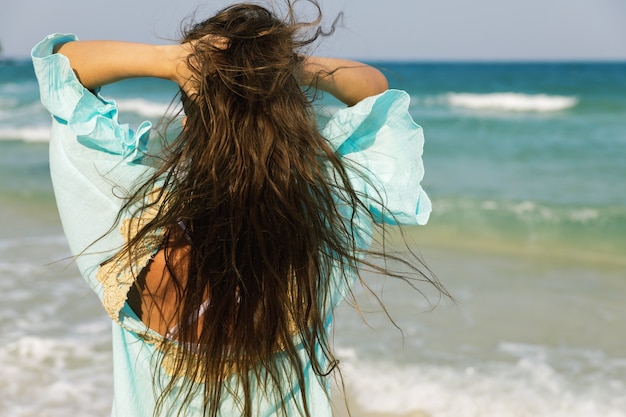 Foto giovane donna che indossa un bel vestito blu sta camminando in riva al mare