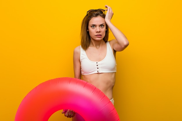 Young woman wearing bikini holding an inflatable donut being shocked, she has remembered important meeting.