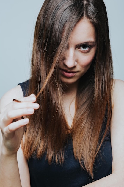 Young woman wearing black dress holding hair and looking at camera Vertical studio shot